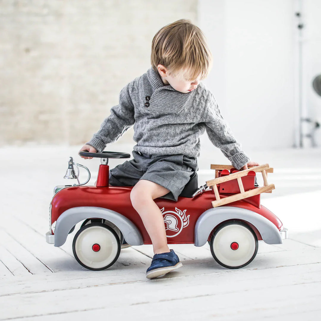 Child sitting on a Baghera speedster red toy fire truck indoors