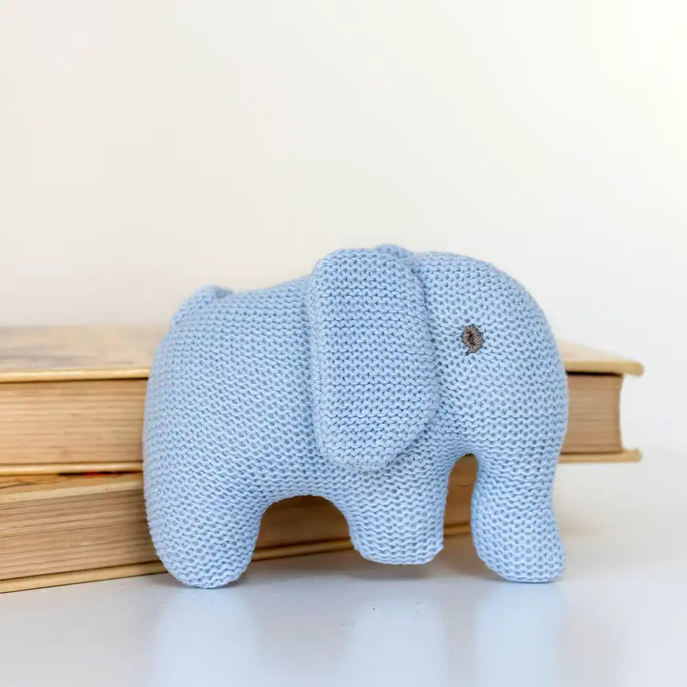 Blue Best Years knitted organic cotton elephant baby rattle, soft and eco-friendly infant toy in front of books.