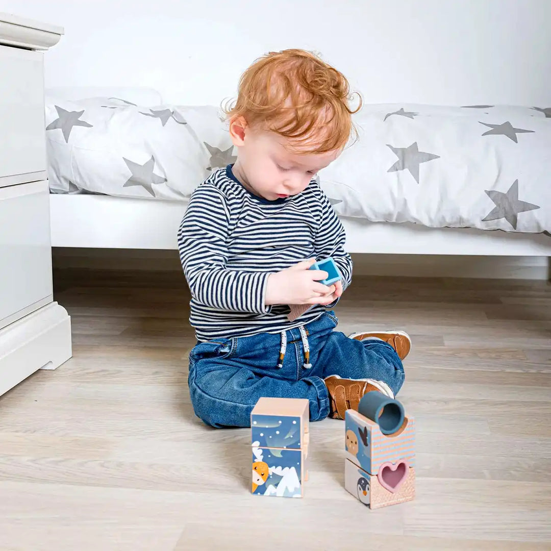 Child playing with a Bigjigs Toys arctic tower puzzle on a wooden floor in a bedroom.