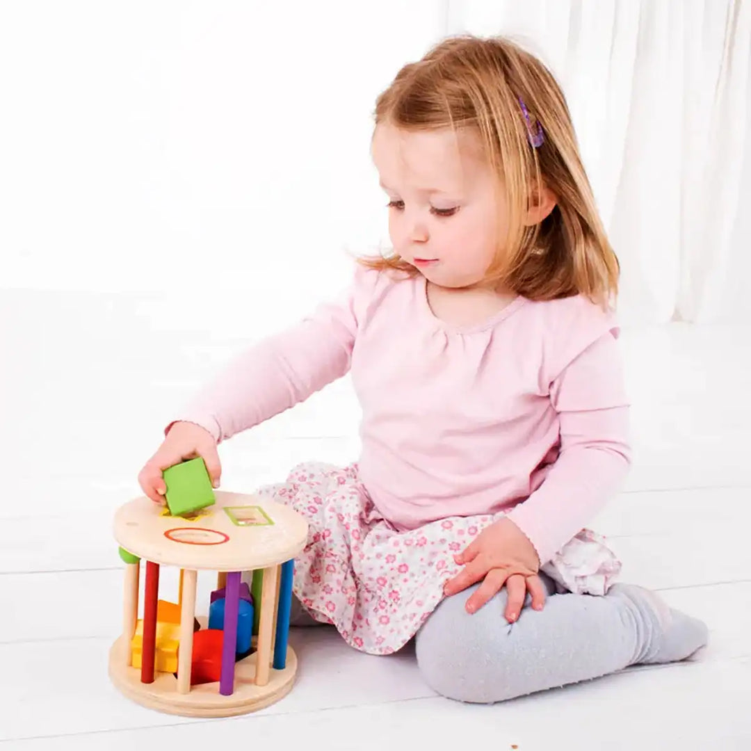 Child playing with a Bigjigs Toys wooden first rolling shape sorter on a white floor