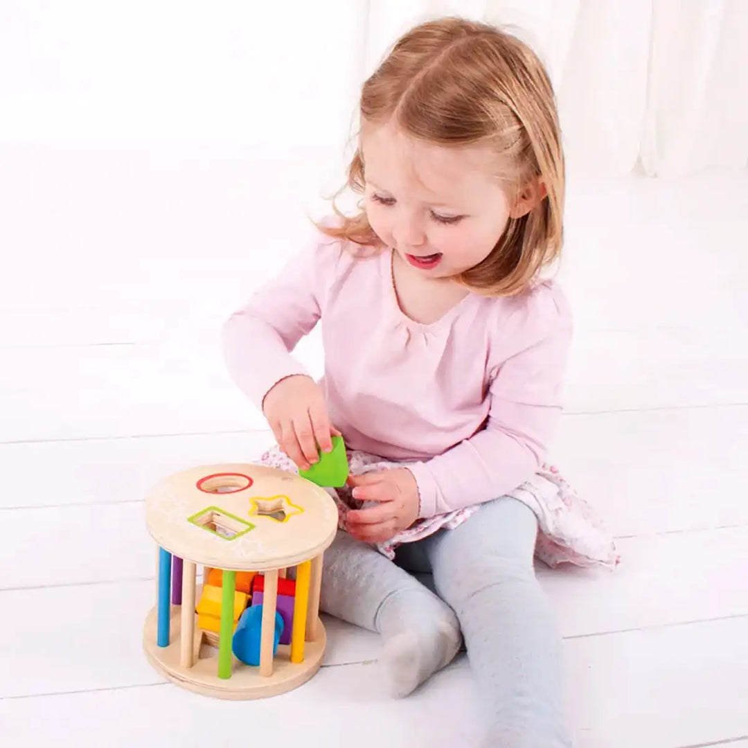 Child playing with a Bigjigs Toys wooden first rolling shape sorter on a white floor