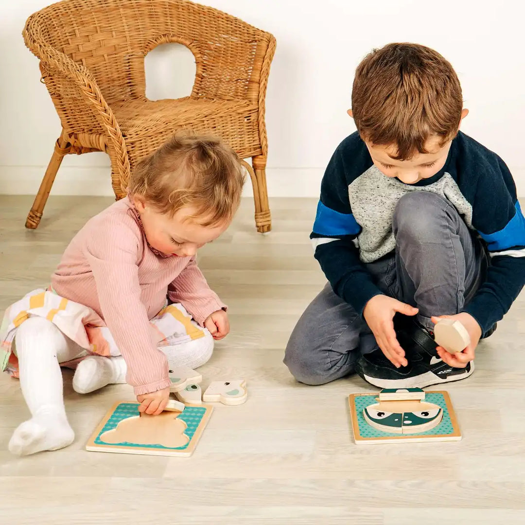 Two children playing with Bigjigs Toys wooden chunky puzzles on a wooden floor.
