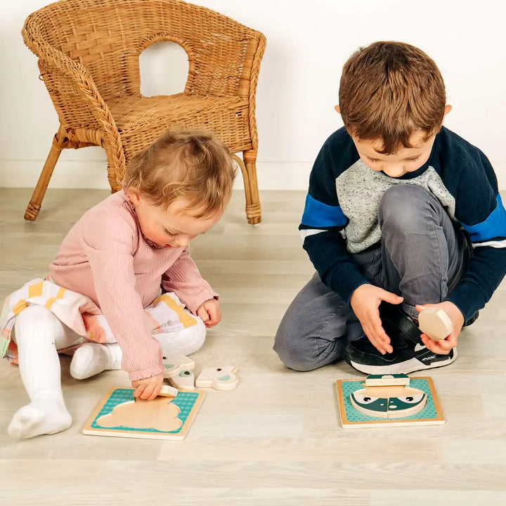 Two children playing with Bigjigs Toys wooden chunky puzzles on a wooden floor.