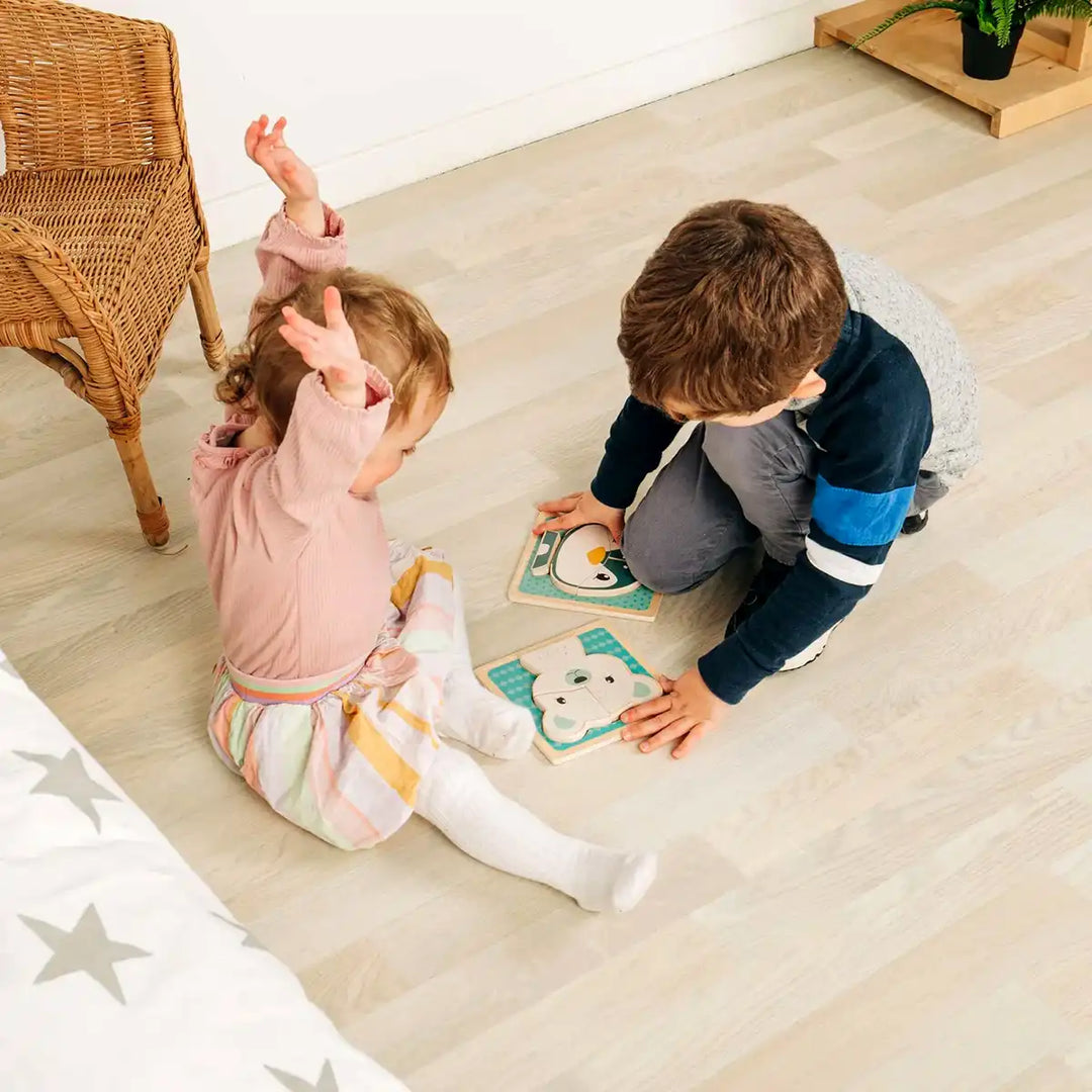 Two children playing with Bigjigs Toys wooden chunky puzzles on a wooden floor.