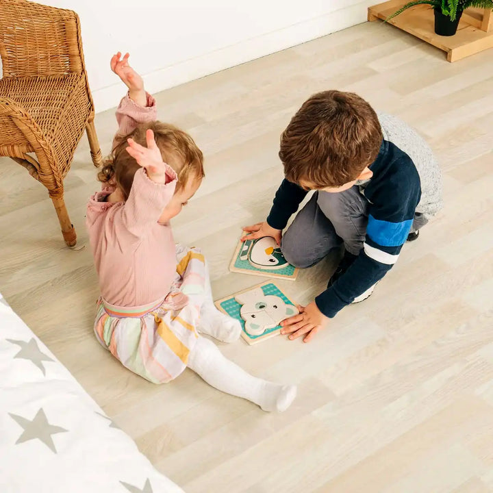 Two children playing with Bigjigs Toys wooden chunky puzzles on a wooden floor.