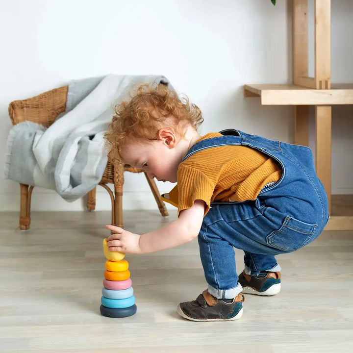 Child playing with a Bigjigs toys colourful silicone stacking cat toy on a wooden floor.