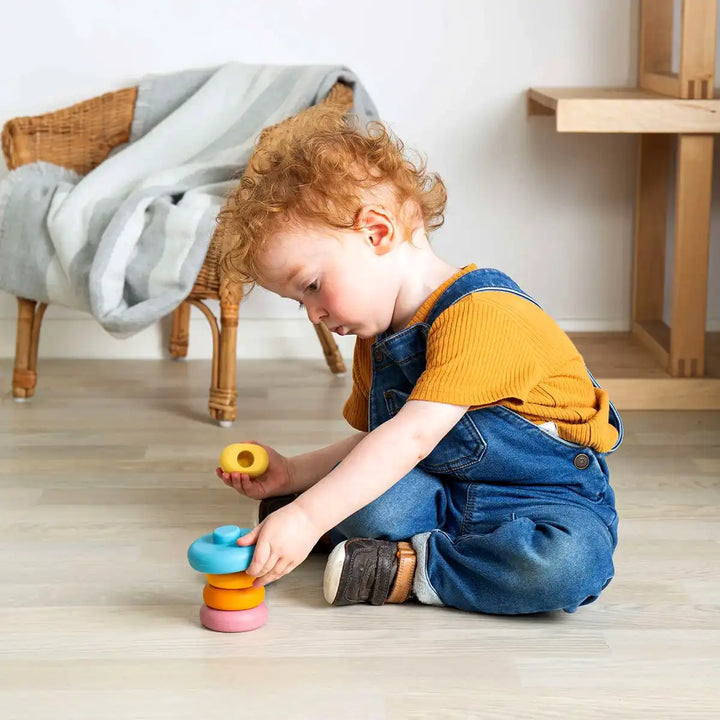 Child playing with a Bigjigs toys colourful silicone stacking cat toy on a wooden floor.