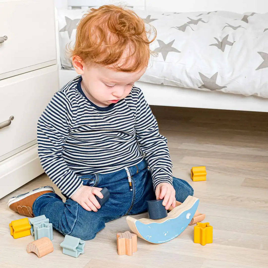Child playing with a Bigjigs Toys wooden moon balance stacker toy on a wooden floor.