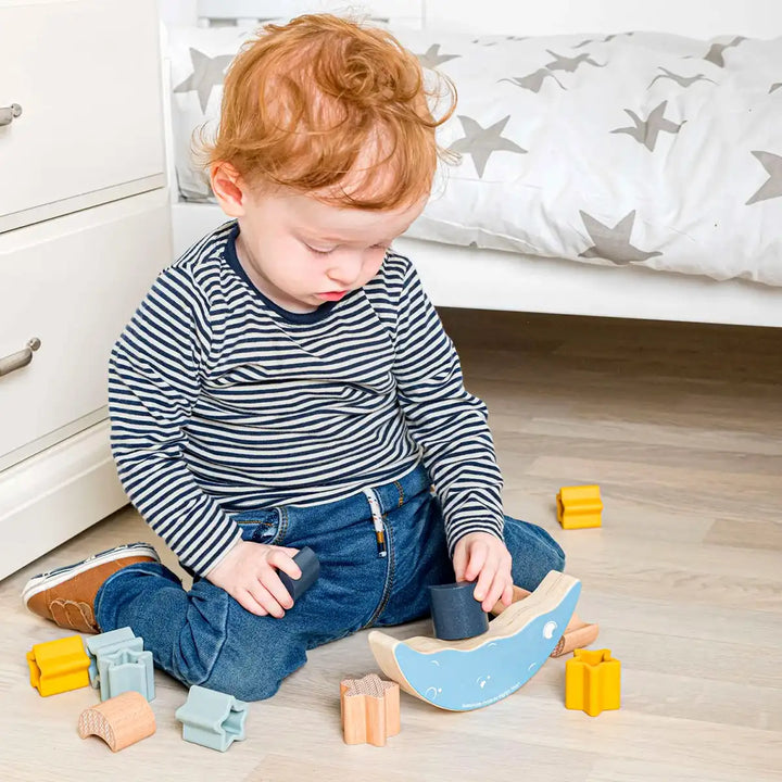 Child playing with a Bigjigs Toys wooden moon balance stacker toy on a wooden floor.