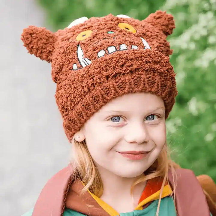 Child wearing a brown knitted Blade & Rose Gruffalo hat with a cartoon face design, outdoors.