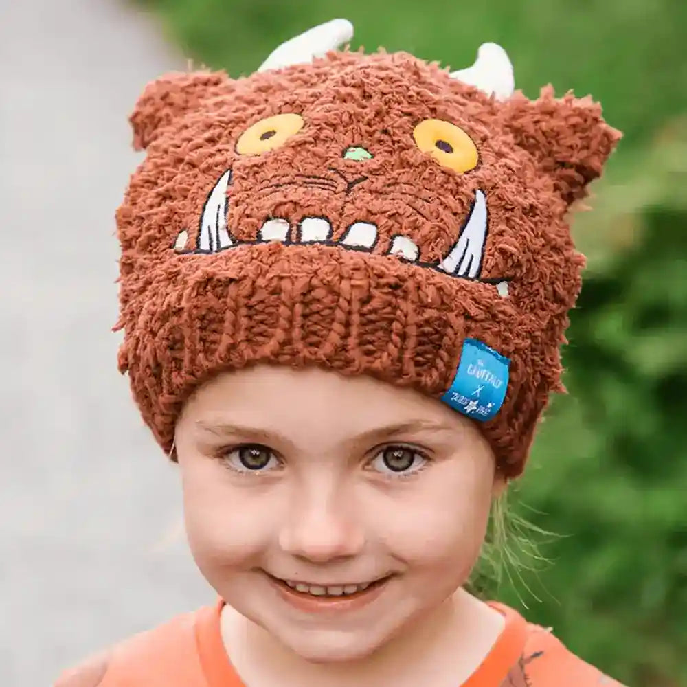 Child wearing a brown knitted Blade & Rose Gruffalo hat with a cartoon face design, outdoors.