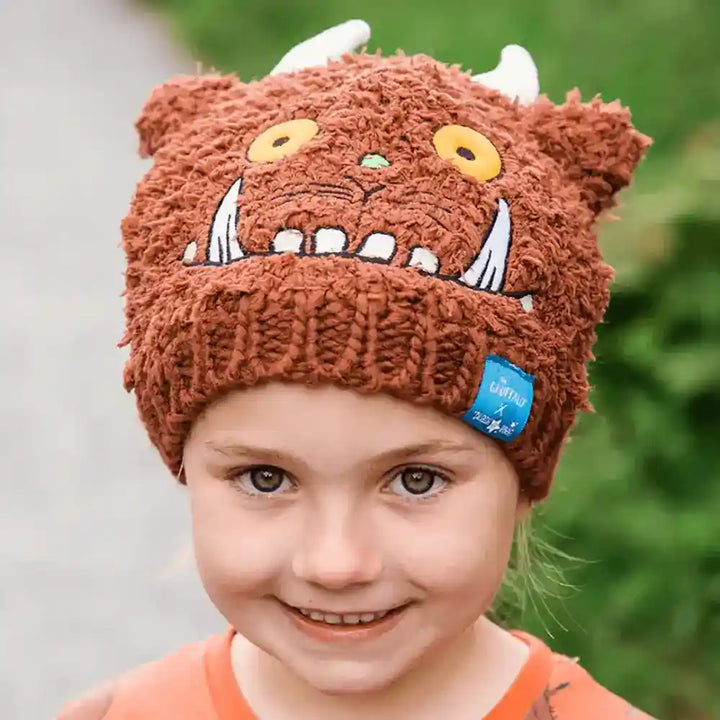Child wearing a brown knitted Blade & Rose Gruffalo hat with a cartoon face design, outdoors.