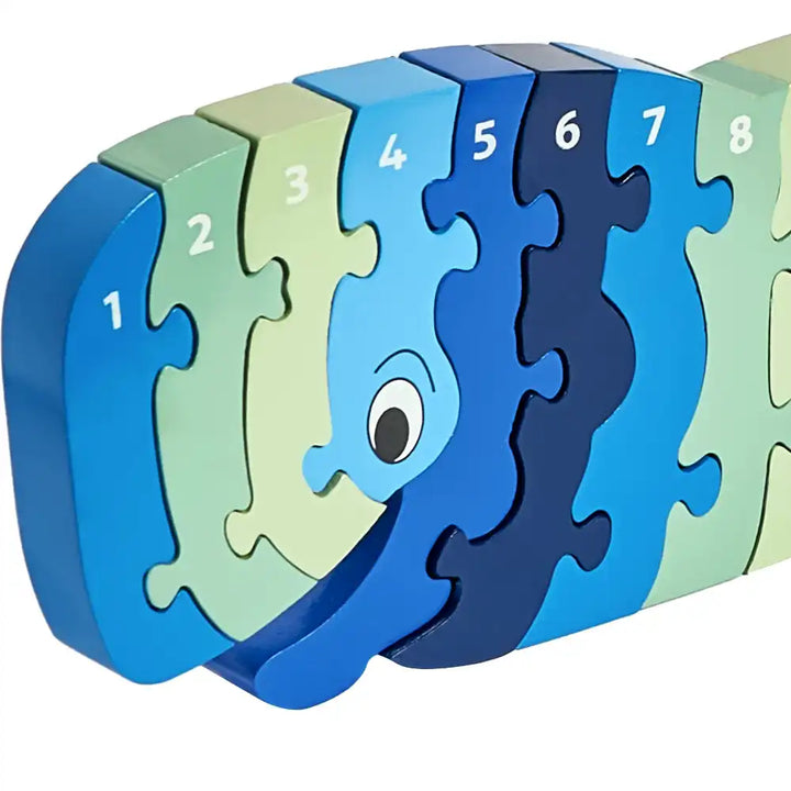 A colourful Lanka Kade wooden number puzzle toy shaped like a whale, featuring numbered pieces in shades of blue, navy, light blue, and pale green on a white background.