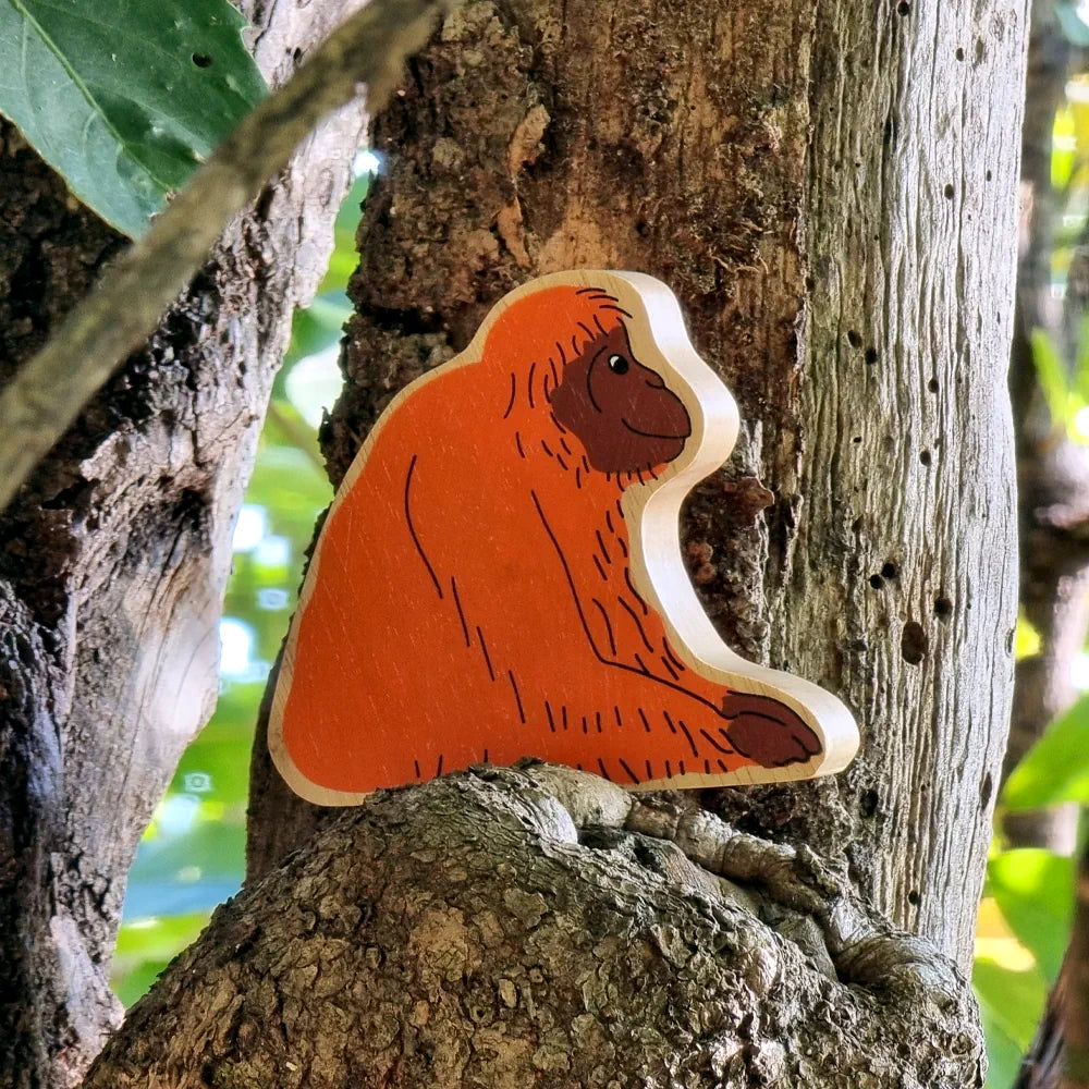 Lanka Kade handcrafted wooden orangutan figure featuring a bright orange painted body, dark brown face and paw, and natural light wood edges, displayed on a textured tree trunk.