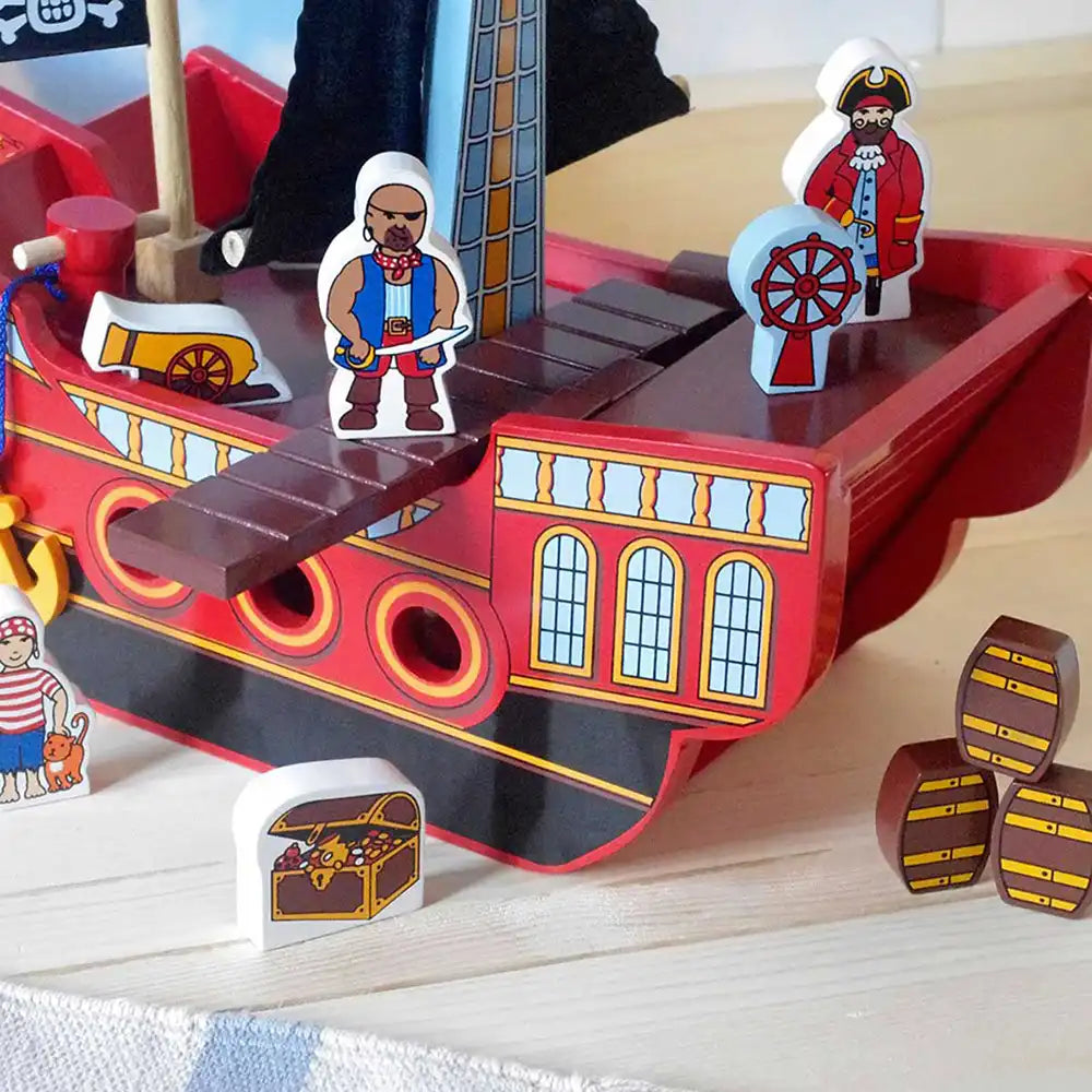 Lanka Kade red and black pirate ship toy with colourful wooden pirate figures, a treasure chest, barrels, and a wheel on a light wood tabletop.