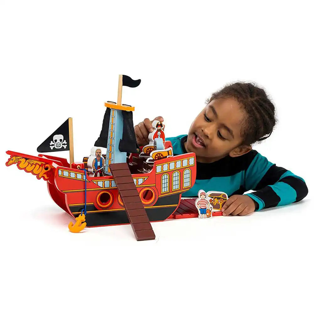 A young child wearing a teal and black striped shirt plays with a red and black Lanka Kade pirate ship toy set with small character figures on a white background.