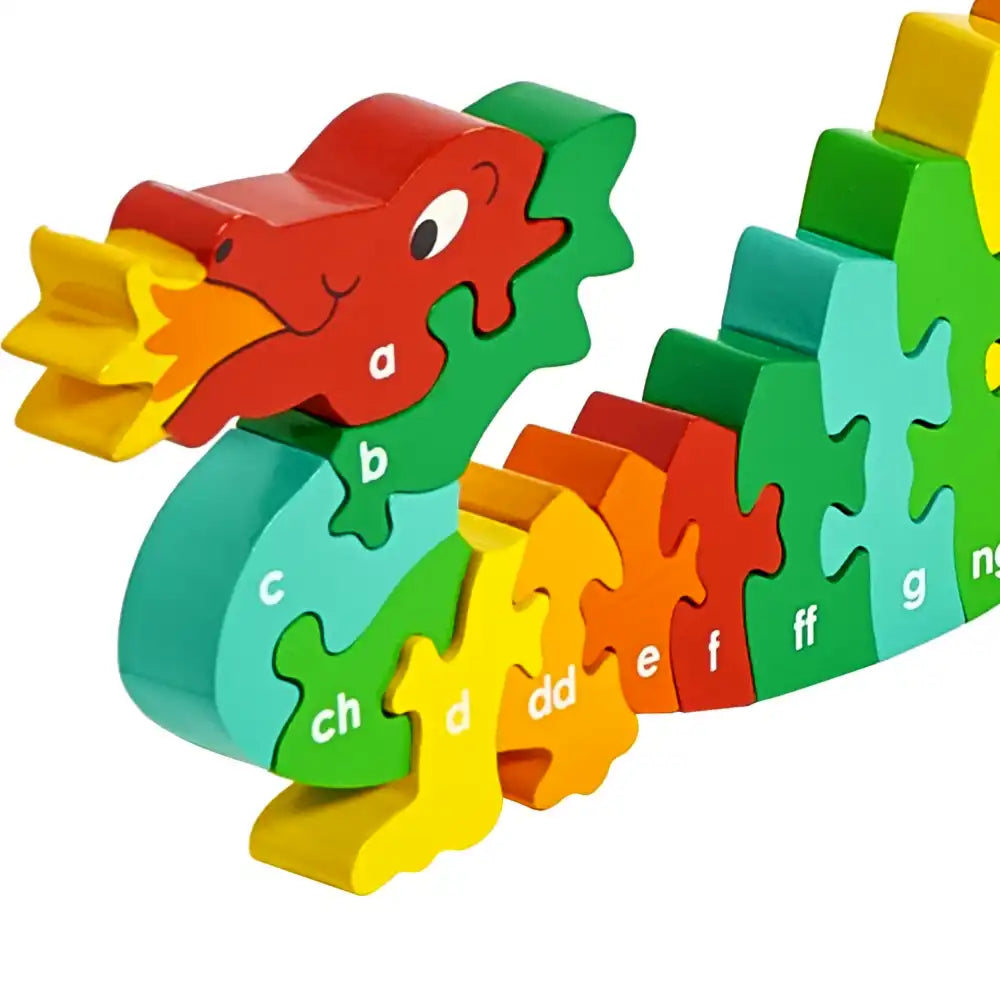 A colourful Lanka Kade wooden Welsh alphabet dragon puzzle toy on a plain white background. The toy is made of interlocking puzzle pieces shaped like a dragon, with each piece labelled with a lowercase alphabet letter from a to n.