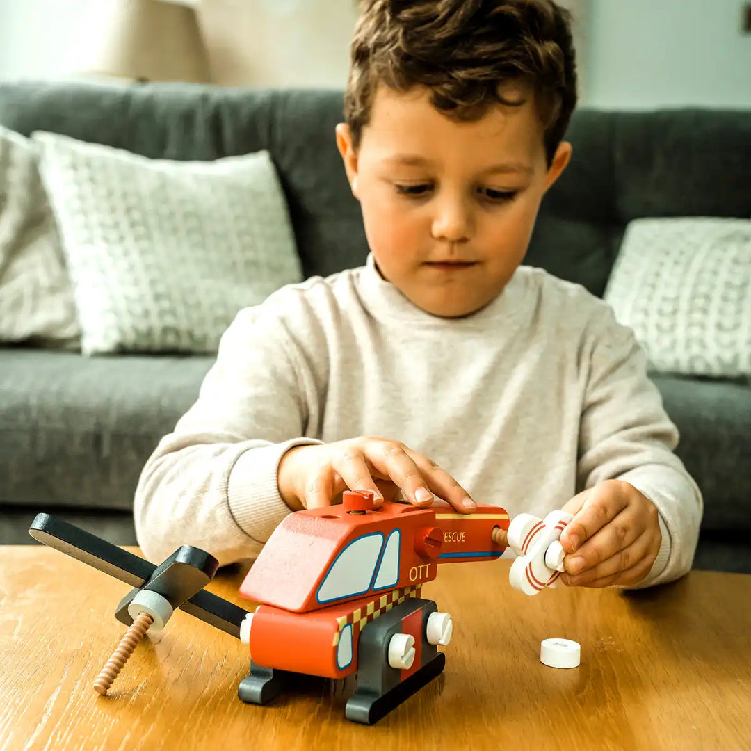 Child playing with an Orange Tree Toys buildable helicopter on a wooden table