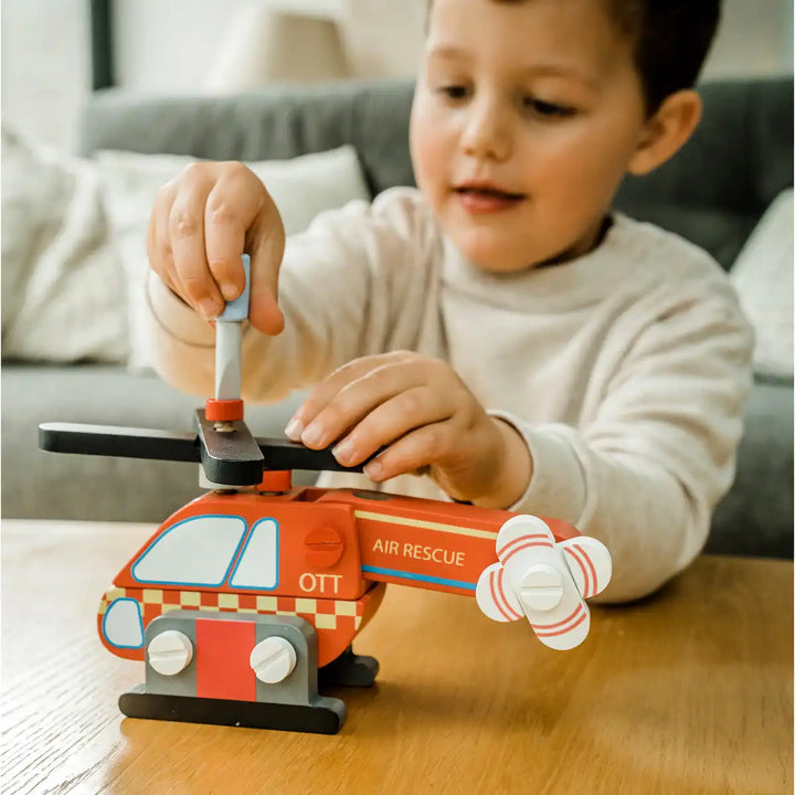 Child playing with an Orange Tree Toys buildable helicopter on a wooden floor.