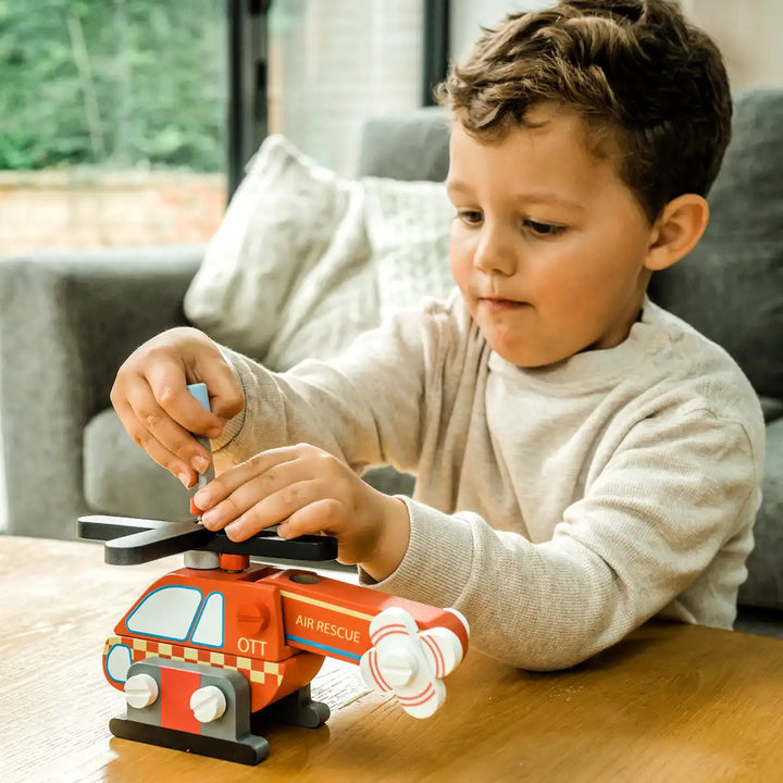 Child playing with an Orange Tree Toys buildable helicopter on a wooden table.