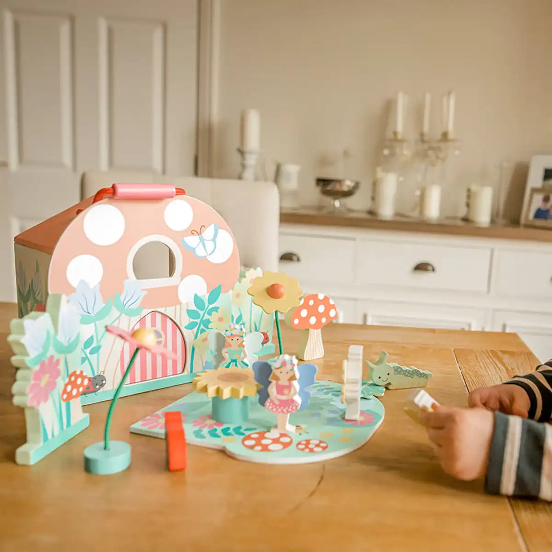 Child playing with an Orange Tree Toys fairy house play set toy on a wooden table with a kitchen in the background