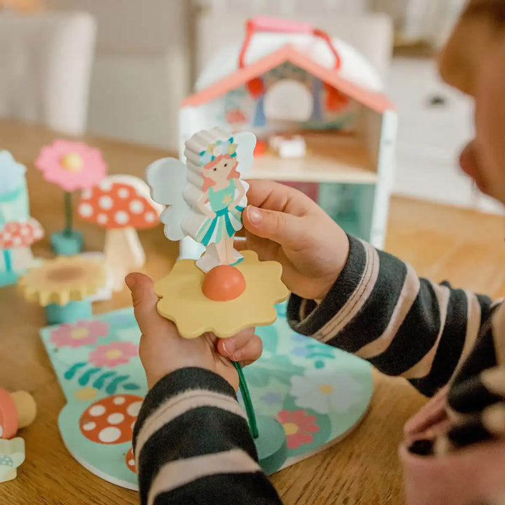 Child playing with an Orange Tree Toys fairy house play set toy on a wooden floor with toys in the background