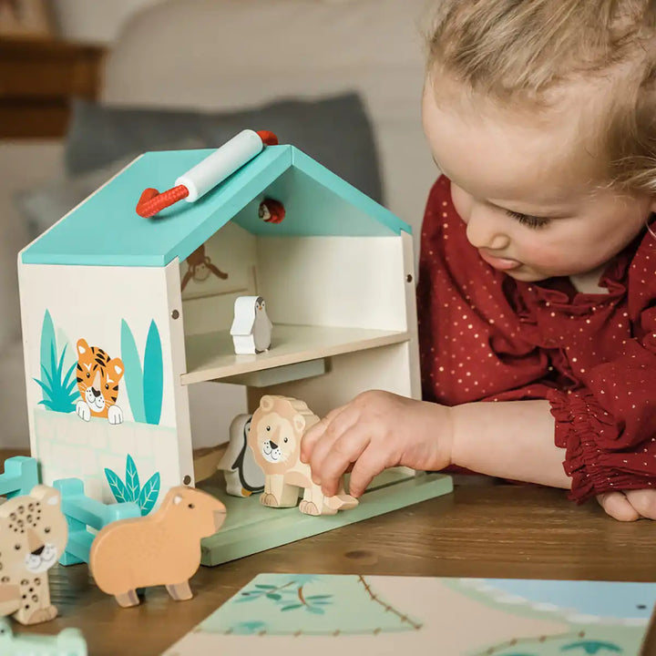 Child playing with an Orange Tree Toys wooden zoo play set with house and animal figures on a table.