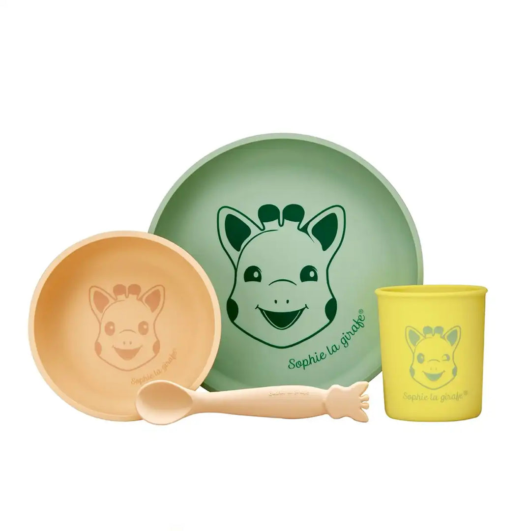 Sophie La Girafe silicone children's tableware set with yellow cup, green plate, beige bowl, and spoon on a white background