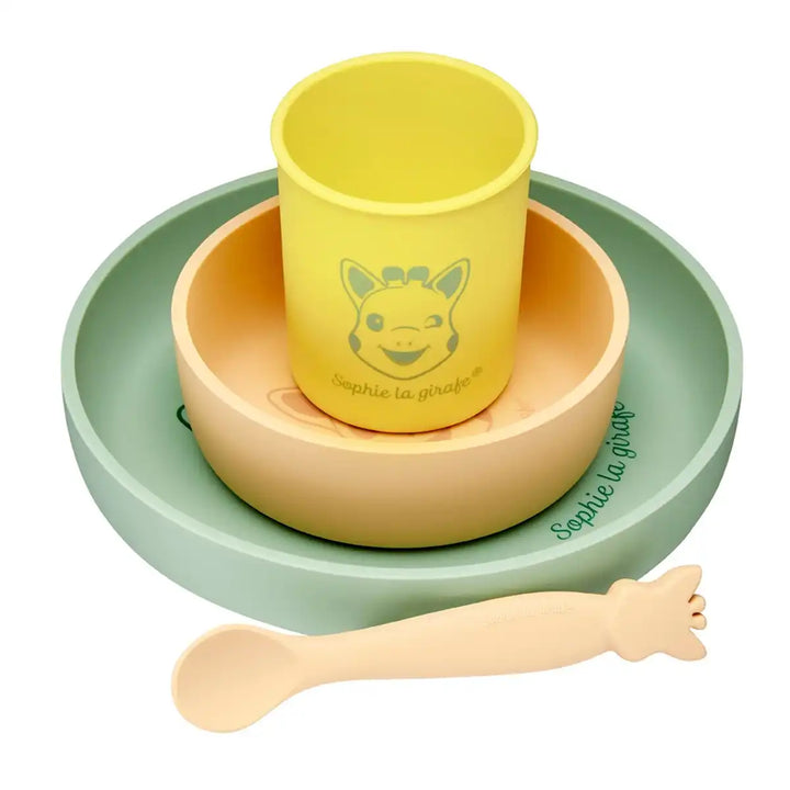 Sophie La Girafe silicone children's tableware set with yellow cup, green plate, beige bowl, and spoon on a white background