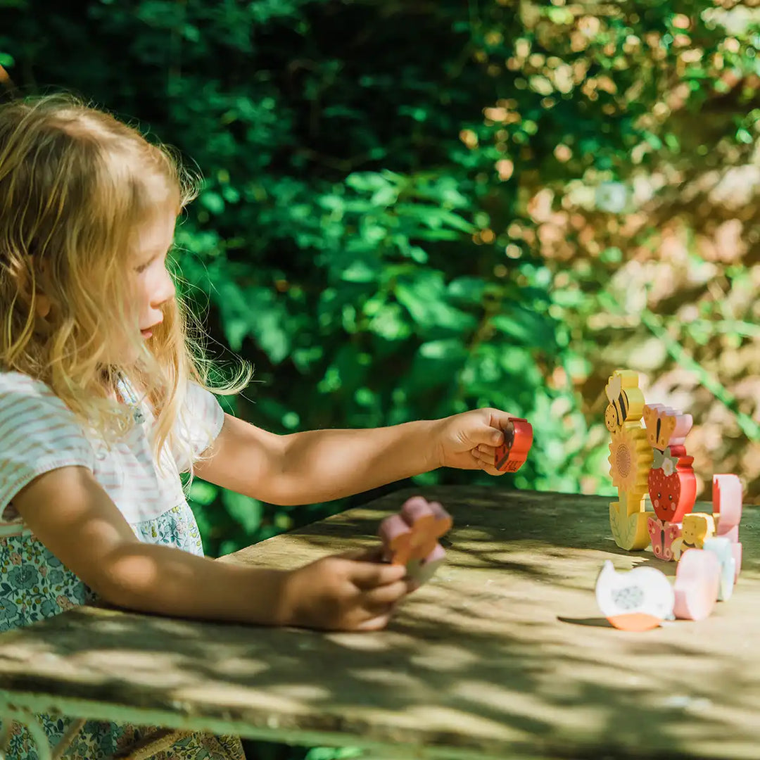 Child playing with Orange Tree Toys stacking spring garden set at a wooden table outdoors